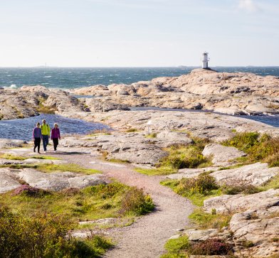 Grupp går vandringsled på Marstrandsön med havet och fyren i